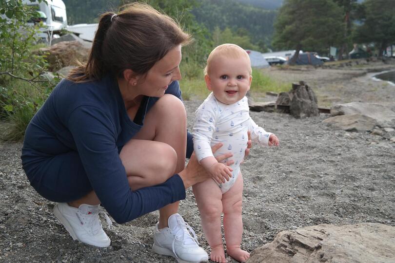 Silje sitter på huk og holder sønnen Oskar, på stranden.