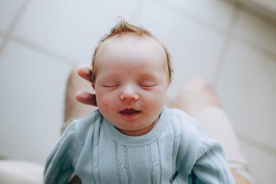 Sovende baby med mørkt hår som står rett opp, blir holdt av en voksen hånd.