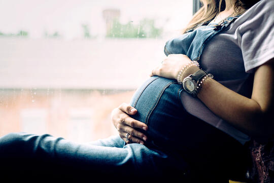 Gravid kvinne sitter i vinduskarm, holder seg på magen