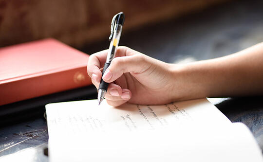 Illustrasjonsbilde av hånd som skriver med penn i en bok.