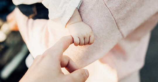 Liten jentes barnehånd holder fast i fingeren til voksen hånd