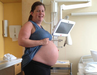 Kristin viser fram sin store gravide mage og smiler.