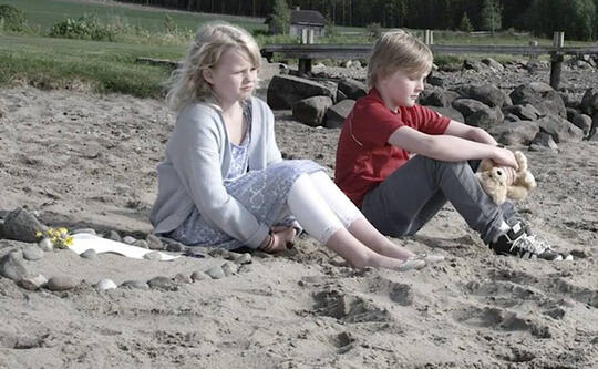En jente og en gutt sitter ved siden av hverandre på stranda.