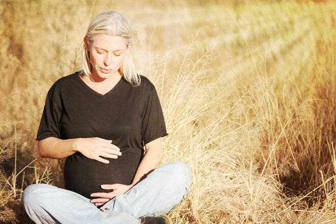 Gravid kvinne sitter i gresset og holder rundt magen..