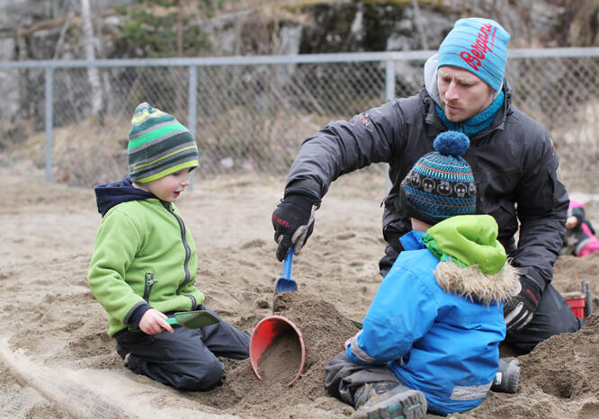 To små barn leker i sandkasse med en voksen mann.