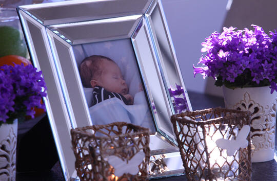 Bilde av baby i ramme står sammen med tente lys og blomster 