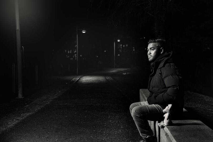 Mann sitter på benk i mørket