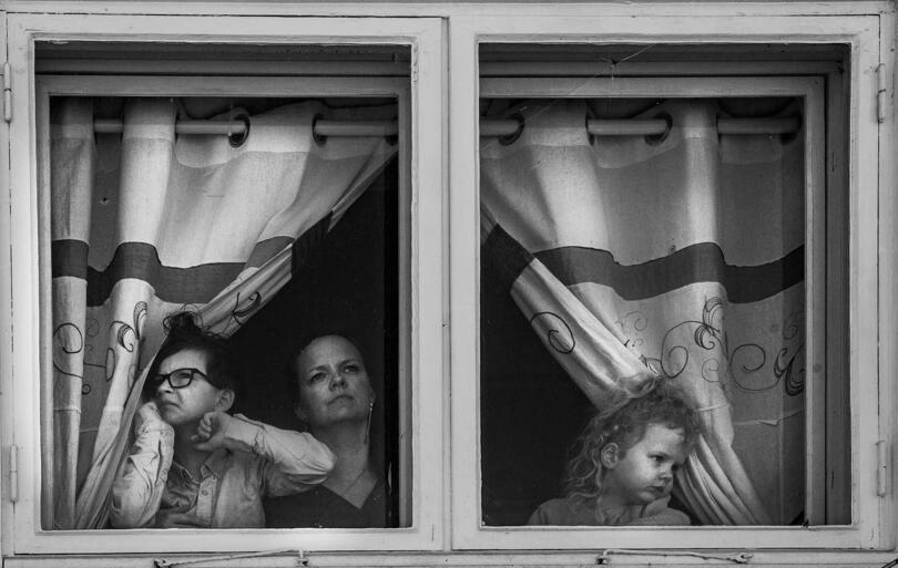 Mor og to barn titter ut gjennom et vindu