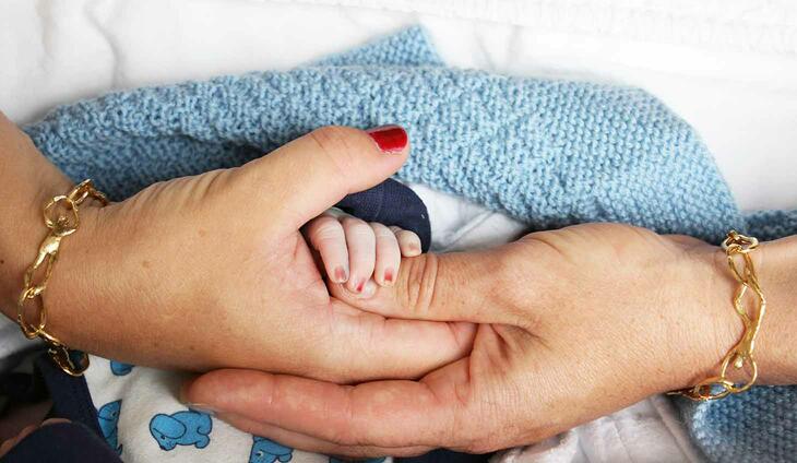 To mammaers hender holder nyfødt hånd.