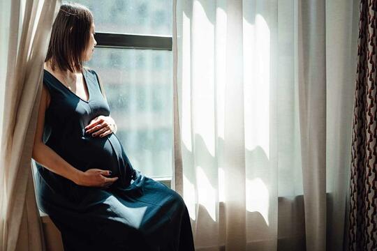 Gravid kvinne sitter i en vinduskarm og ser ut.
